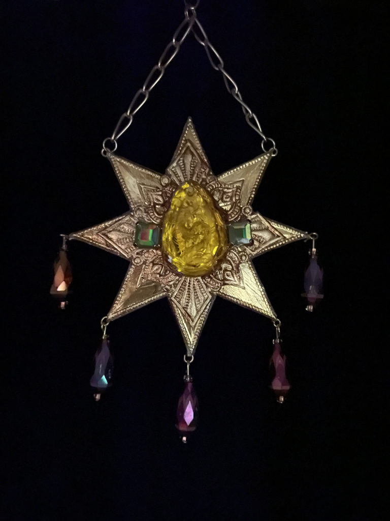 Right at home amidst the elaborate costumes of carnival in Venice is this pendant. An octagram in shape, iridescent glass drops dangle from the star points and a topaz colored crystal with a dragon carving is at the center.