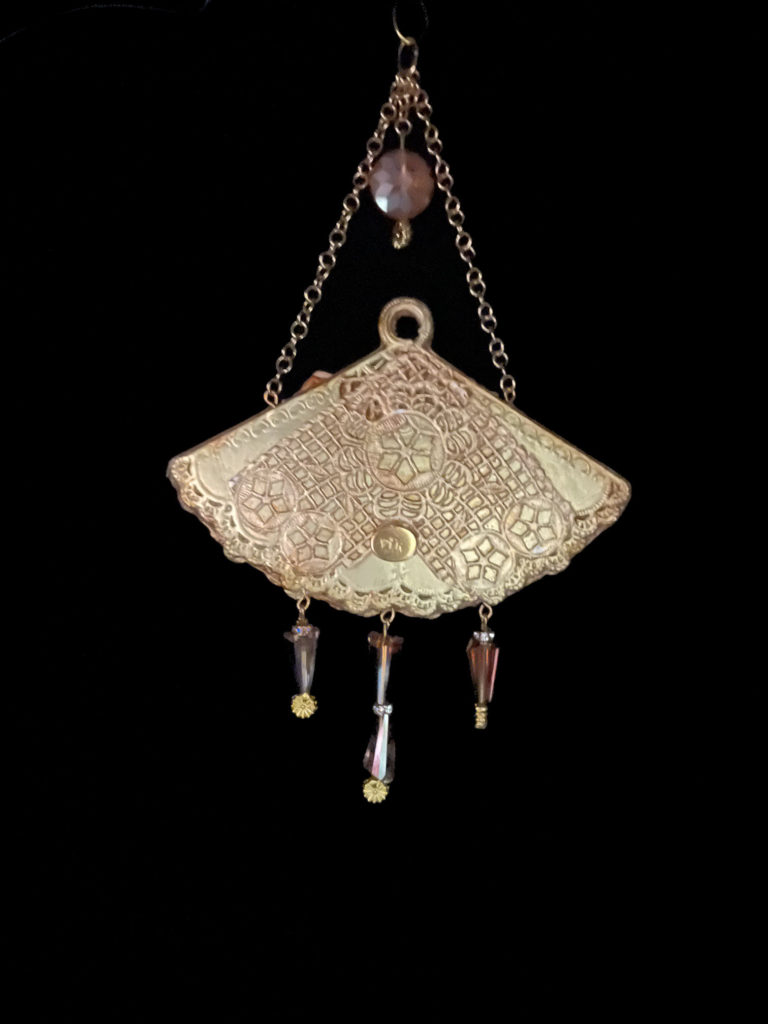 A gold embellished fan with an intaglio cameo mounted on butterfly wings. Cone-shaped crystals dangle from the bottom and it hangs beautifully from a cream-colored velvet rope choker