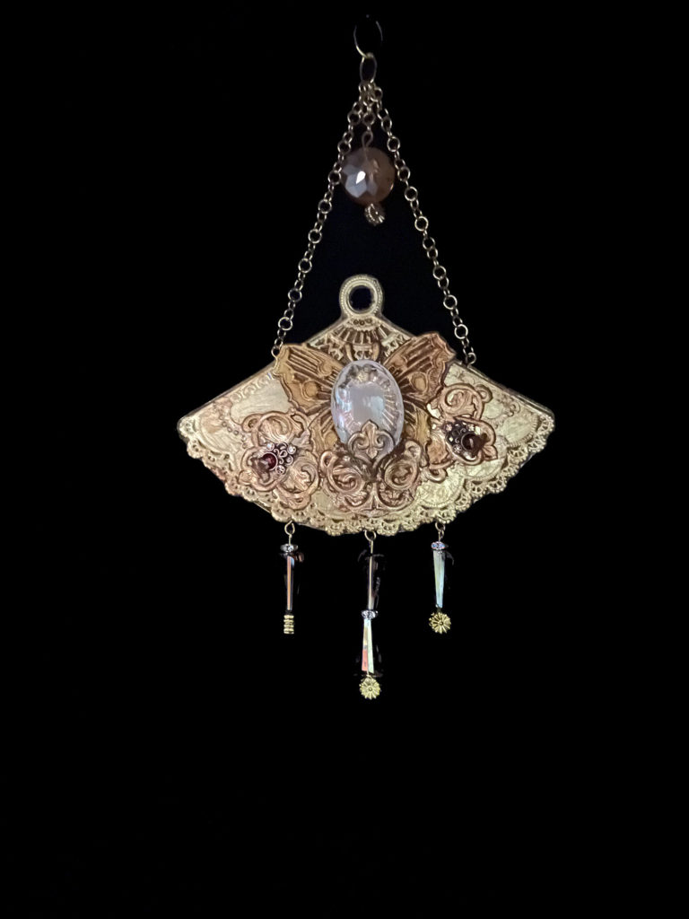 A gold embellished fan with an intaglio cameo mounted on butterfly wings. Cone-shaped crystals dangle from the bottom and it hangs beautifully from a cream-colored velvet rope choker