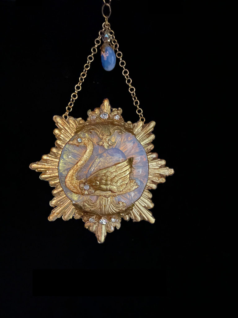 A graceful Swan floats on a golden sunburst embellished with glowing Opalite and clear rhinestones and suspended from a cream-colored velvet choke