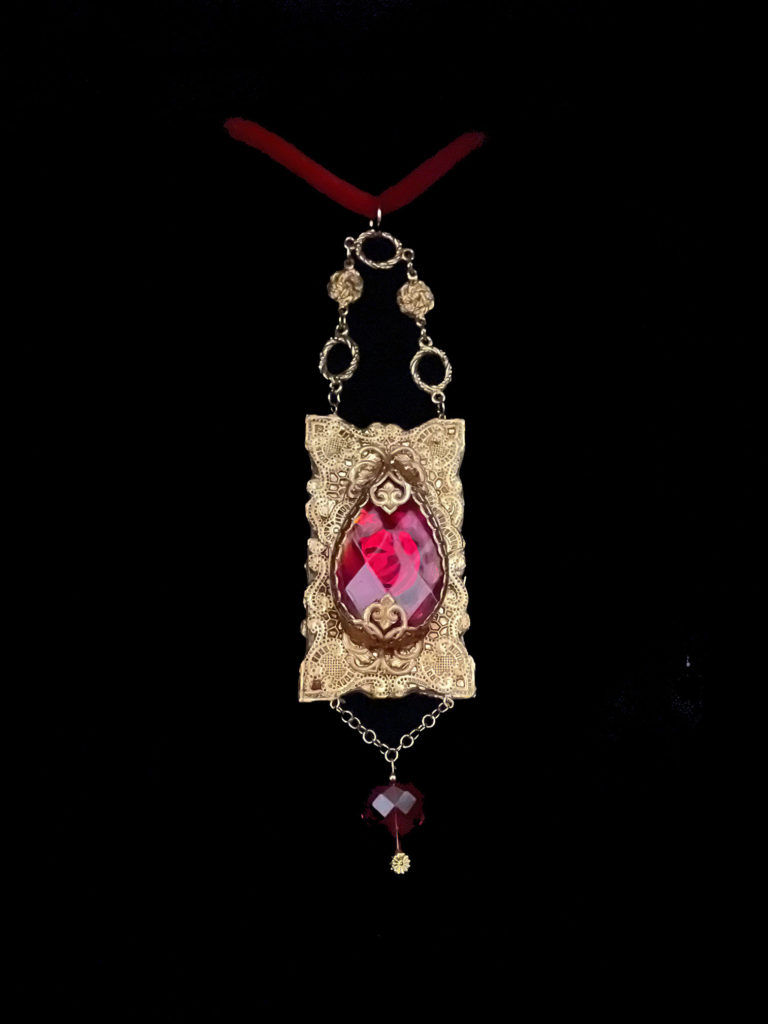 Fit for a queen, a large red almond-shaped crystal is the centerpiece with a smaller red heart crystal suspended by a chain