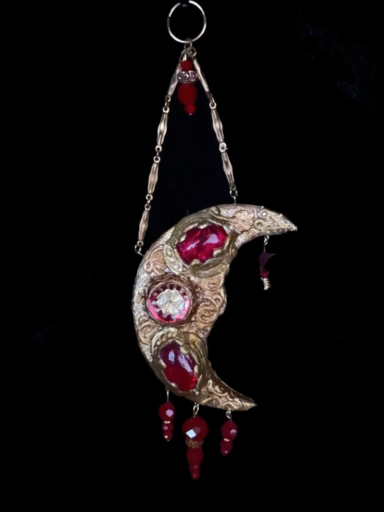 The Blood Moon glows red in the shadow of the sun, its beauty not to be eclipsed. Red velvet beads, glass cabochons, and a glass dome are added enhancements.