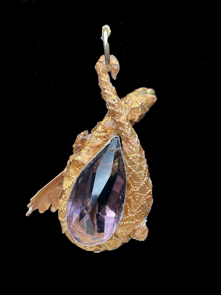 Encrusted with Amethyst chips and mounted on an Amethyst-colored crystal, this dragon is the protector of spirituality. Serene and peaceful in nature. He balances emotions from a gold ruched velvet choker.