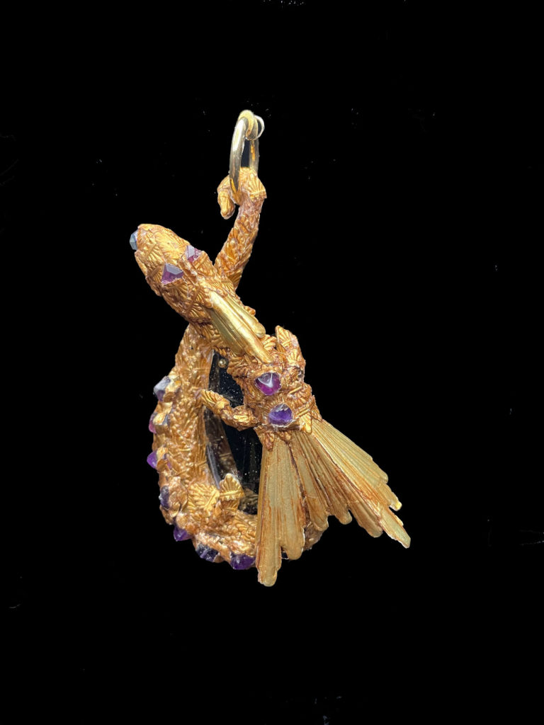 Encrusted with Amethyst chips and mounted on an Amethyst-colored crystal, this dragon is the protector of spirituality. Serene and peaceful in nature. He balances emotions from a gold ruched velvet choker.