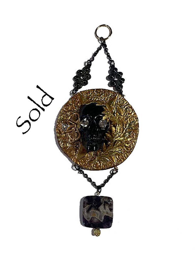 Front of pendant - A black skull on a gold background with additional small findings.